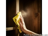 The image shows a person's hand holding a yellow microfiber cloth and wiping a wooden door. The person is using the cloth to...