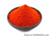 The image shows a small black bowl filled with a pile of red chili powder. The powder appears to be finely ground and has a v...