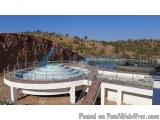 The image shows a large circular structure with a white exterior and a blue roof. It appears to be a water treatment plant or...