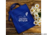 The image shows a blue tote bag with the words "Responsible Citizen" written in white on the front. The bag has two handles a...