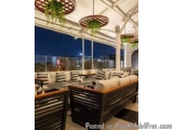 The image shows a modern outdoor seating area with a view of the city at night. The seating area is furnished with white sofa...