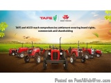 The image shows a group of red tractors parked in a row on a dirt field. The tractors are of different sizes and models, with...