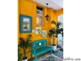 The image shows a small porch with a bright yellow wall and a blue bench. The bench is painted in a turquoise color and has a...