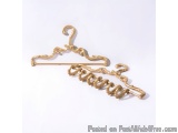 The image shows a gold-colored hanger with a curved design. The hanger is made of metal and has a hook at the top for hanging...