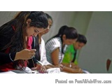 The image shows a group of four young women sitting at a desk in a classroom. They are all focused on their work, with one wo...