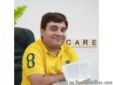 The image is a portrait of a young man sitting at a desk. He is wearing a yellow polo shirt with the number 8 on it and is sm...