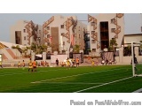 The image shows a soccer field with a group of people playing soccer on it. The field is covered in artificial turf and there...
