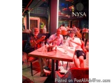 The image shows three men sitting at a table in a restaurant named NYSA. They are all smiling and appear to be enjoying their...