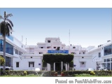 The image shows a large white building with a blue signboard in front of it. The building appears to be a government or gover...