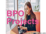The image shows a young woman sitting at a desk with a laptop in front of her. She is wearing a black top and has long brown...
