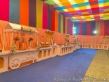 The image shows a long table set up in a colorful tent-like setting. The tent is decorated with a rainbow-colored striped pat...