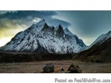 The image shows a beautiful landscape of a mountain range with snow-capped peaks. The sky is cloudy and the sun is setting, c...