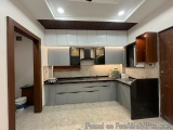 The image shows a modern kitchen with a large island in the center. The kitchen has a gray countertop with a black countertop...
