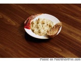 The image shows a plate of macaroni and cheese on a wooden table. The plate is white and round, and it is placed on a white p...