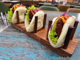 The image shows three buns on a wooden tray. The buns are filled with a dark brown meatball, topped with lettuce, red cabbage...