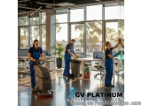 The image shows a group of four people in an office setting. They are all wearing blue overalls and are cleaning the floor wi...