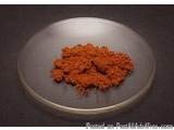 The image shows a small round plate with a black background. On the plate, there is a pile of red chili powder. The chili pow...