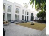The image shows a modern, luxurious outdoor living space with a large white building in the background. The building has mult...