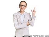 The image is a portrait of a young woman wearing a light grey blazer and glasses. She is standing with her arms crossed and i...