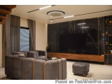 The image shows a modern living room with a large flat-screen TV mounted on the wall. The TV is black and has a wooden frame....