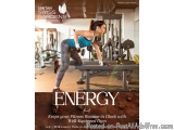The image shows a young woman working out in a gym. She is wearing a blue tank top and grey leggings and is holding a pair of...