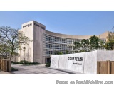 The image shows a modern building with a curved facade. The building is made of light-colored concrete and has the word "Cour...