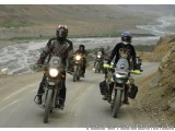 The image shows a group of motorcyclists riding on a winding road in a mountainous area. The road is narrow and narrow, with...