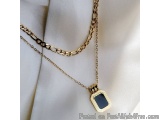 The image shows a gold necklace with a pendant. The pendant is in the shape of a hexagon with a black stone in the center. Th...