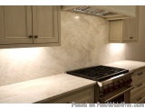The image shows a modern kitchen with a white countertop and a gas stove. The countertop is made of a light-colored marble-li...