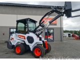 The image shows a Bobcat skid steer loader parked in front of a building. The loader is white and orange in color with the Bo...
