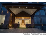 The image shows the entrance of a modern building at night. The building has a large wooden structure with a triangular roof...