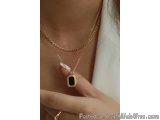 The image shows a close-up of a woman's neck and upper body, with a gold necklace and a ring on her finger. The necklace is m...
