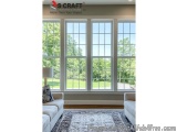 The image shows a large window in a living room with a view of a green lawn and trees outside. The window is made of glass an...
