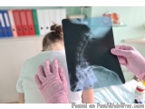 The image shows a person holding an X-ray of a spine. The person is wearing a white t-shirt and pink gloves. The X-rays are b...