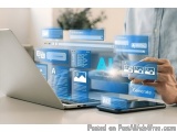 The image shows a person's hand holding a tablet and a laptop on a desk. The laptop screen displays various icons and text re...