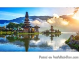 The image is a beautiful landscape of a temple complex in Bali, Indonesia. The temple is located on the shore of a lake, surr...