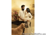 The image shows a young couple standing in a room with a large painting on the wall behind them. The man is wearing a white s...