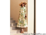 The image shows a young woman standing on a set of stairs. She is wearing a long, flowy dress with a tropical print in shades...