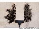 The image shows a black vacuum cleaner on a beige carpet. The vacuum cleaner has a black handle and a black nozzle at the bot...