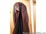 The image shows a brown leather coat hanging on a wooden door. The coat has a collar and long sleeves, and it appears to be m...