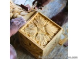 The image shows a person's hands working on a wooden box. The box appears to be made of a light-colored wood and has intricat...
