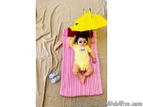 The image shows a baby lying on a pink and white striped blanket on a beige carpeted floor. The baby is wearing a yellow ones...
