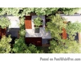 The image is an aerial view of a modern house with a white exterior and a red roof. The house is surrounded by trees and gree...