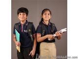 The image shows two young children, a boy and a girl, standing side by side and smiling at the camera. They are both wearing...