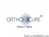 The image is a logo for OrthoCure Clinics I Gyms. The logo is written in a modern, sans-serif font and is in a dark blue colo...