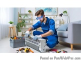In this image, we can see a man wearing a blue uniform and safety goggles, working on an air conditioning unit in a living ro...