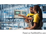 The image shows a man and a woman in a factory setting. They are both wearing yellow t-shirts and are standing in front of a...