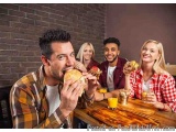 The image shows a group of four young people sitting at a wooden table in a restaurant. They are all smiling and enjoying the...