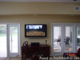 The image shows a living room with a flat-screen TV mounted on the wall above a wooden entertainment center. The TV is turned...