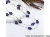 The image shows a long necklace made of silver chain with multiple round, blue stones. The stones are arranged in a circular...